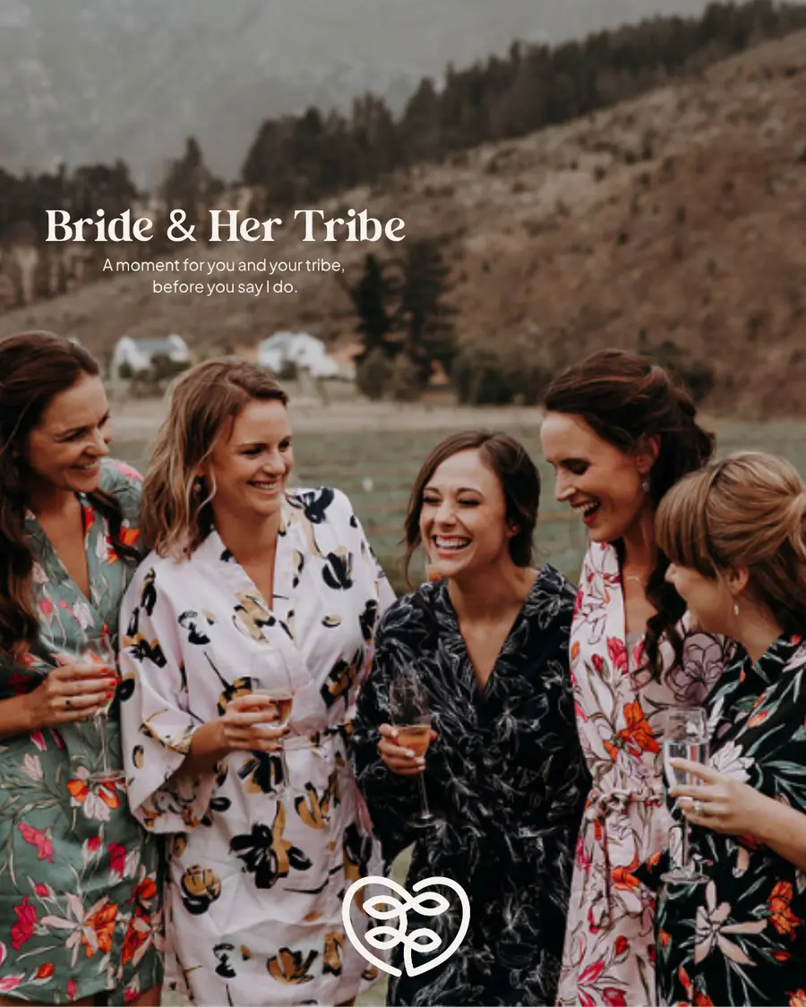 A bride laughing with her bridesmaids, all in floral robes, on the morning of the wedding